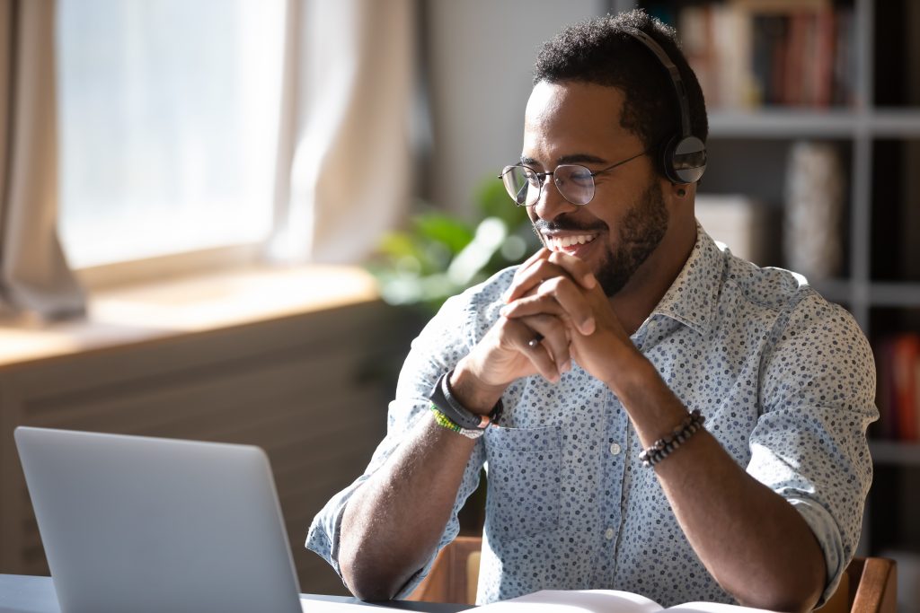 Sempris Happy millennial african american man in glasses wearing headphones, enjoying watching educational webinar on laptop. Smiling young mixed race businessman holding video call with clients partners.